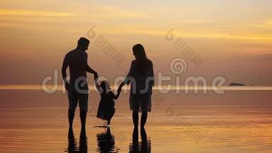 幸福的年轻一家人牵着手，在令人惊叹的金色日落中沿着海岸散步。 家庭假日。 <strong>慢慢慢慢</strong>